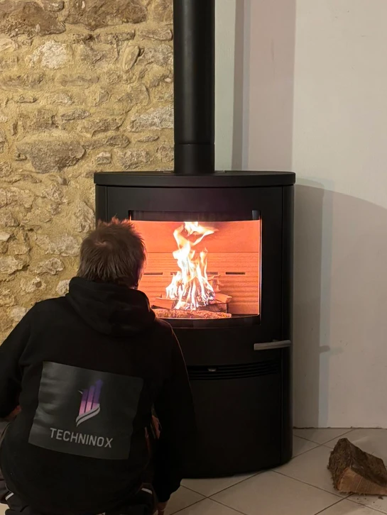 Int&eacute;rieur chaleureux avec po&ecirc;le &agrave; bois en fonctionnement, flammes visibles derri&egrave;re la vitre