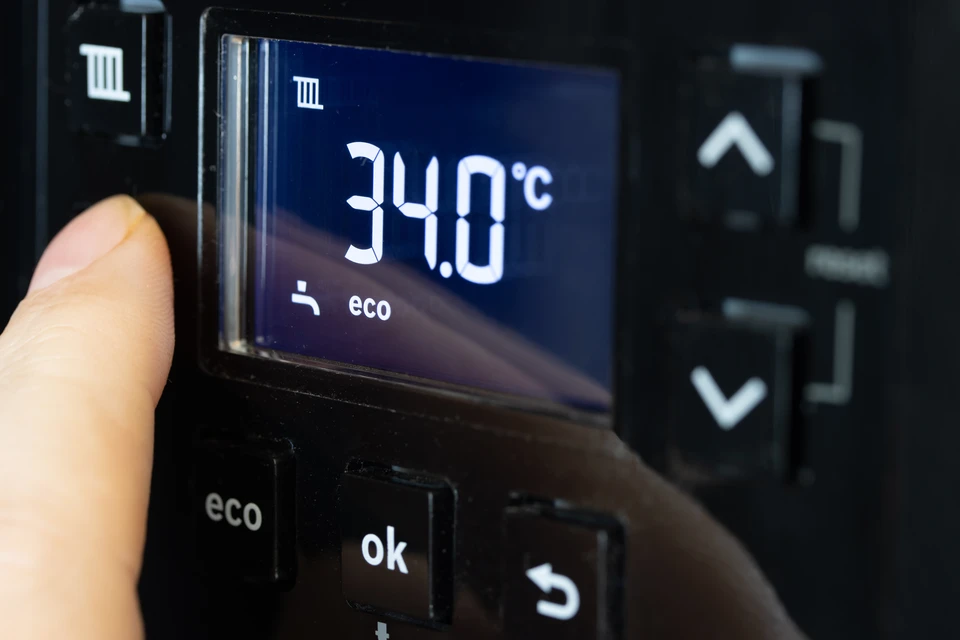 Installateur professionnel en salopette marron et gants bleus montant un conduit de ventilation noir dans les combles d'une habitation